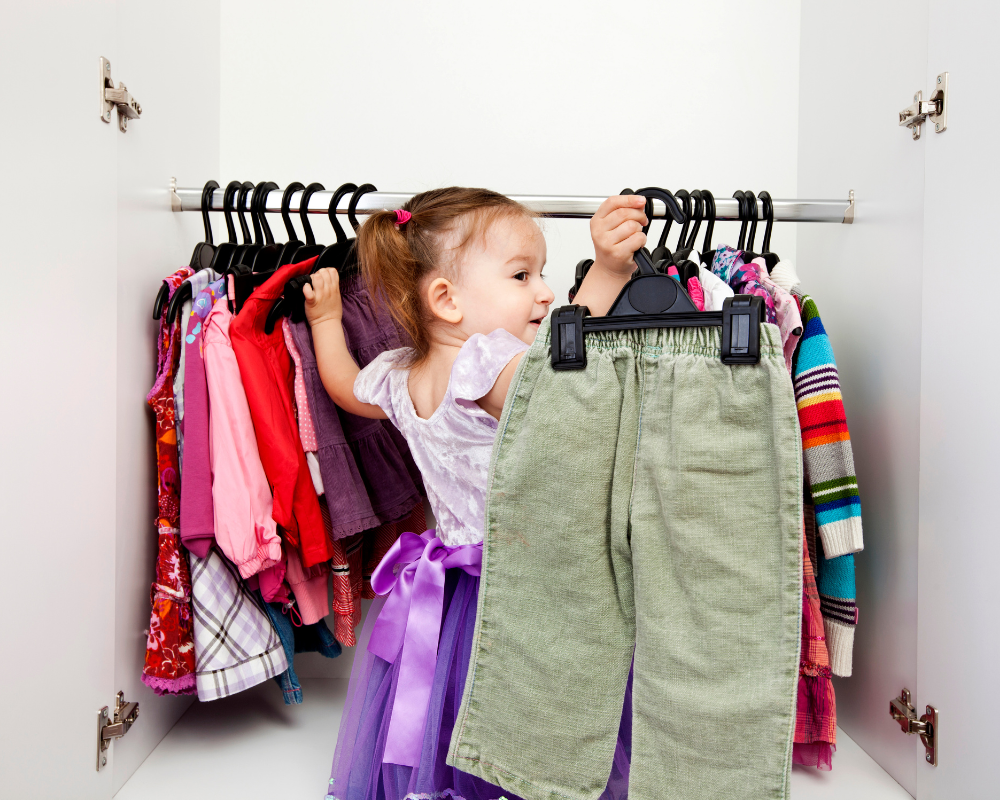 une petite fille dans un placard avec des vêtements sur des cintres